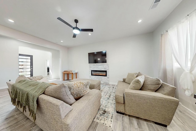 living room with visible vents, recessed lighting, ceiling fan, a glass covered fireplace, and light wood-type flooring