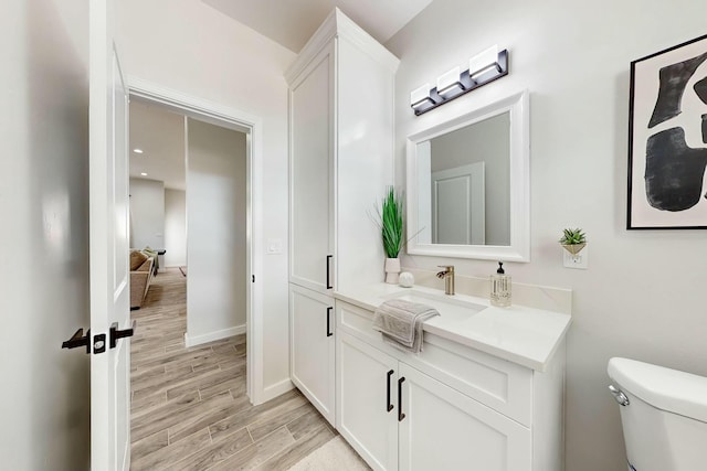 half bath featuring toilet, vanity, baseboards, and wood finished floors