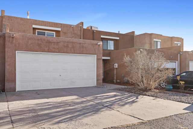 pueblo-style home with stucco siding, driveway, and an attached garage