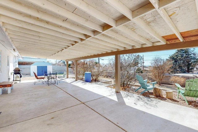 view of patio / terrace featuring a storage unit, an outbuilding, outdoor dining space, fence, and grilling area