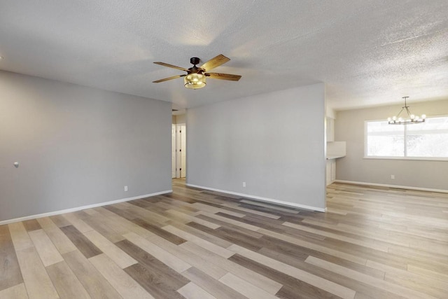 empty room featuring light wood-type flooring, baseboards, a textured ceiling, and ceiling fan with notable chandelier