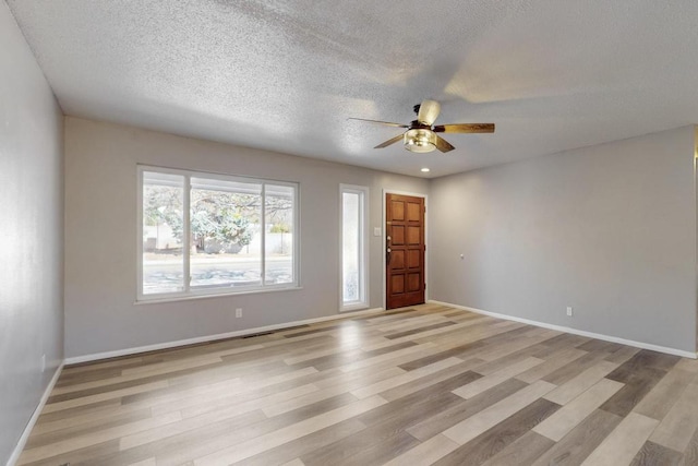 spare room featuring a textured ceiling, a ceiling fan, light wood-style floors, and baseboards