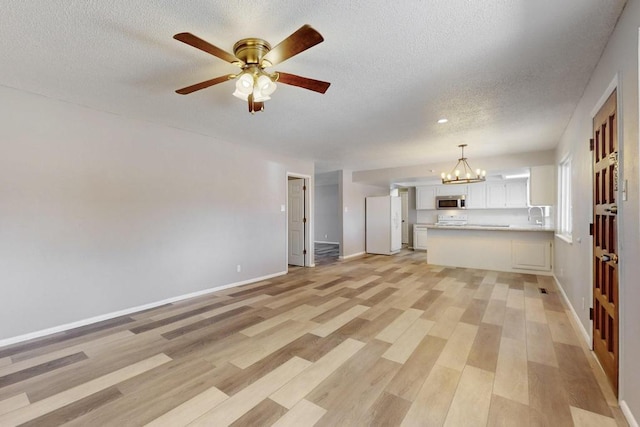 unfurnished living room featuring baseboards, a sink, light wood-style floors, a textured ceiling, and ceiling fan with notable chandelier