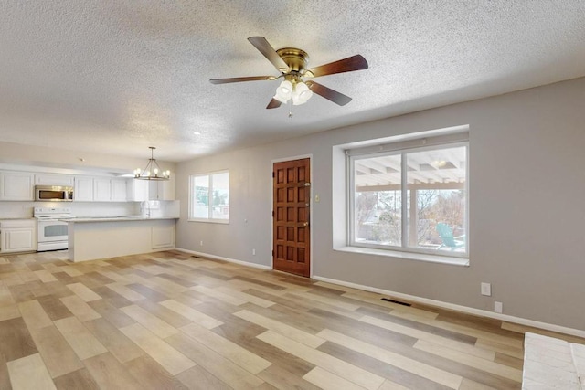 unfurnished living room featuring visible vents, baseboards, ceiling fan with notable chandelier, light wood-style floors, and a textured ceiling