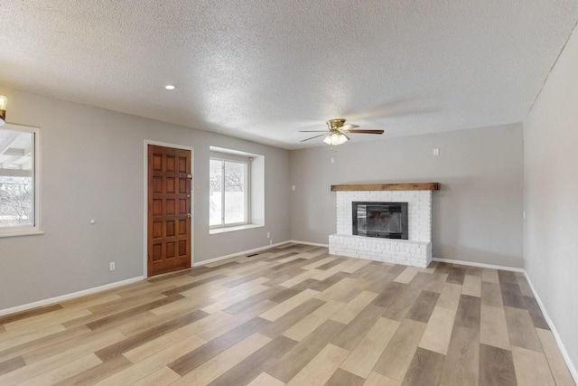 unfurnished living room with light wood finished floors, a brick fireplace, baseboards, and ceiling fan