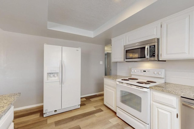 kitchen with appliances with stainless steel finishes, baseboards, a tray ceiling, and light wood-style floors