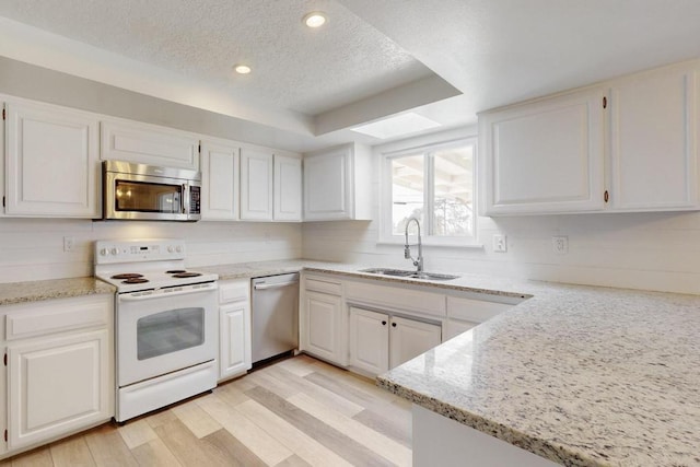 kitchen with a skylight, a sink, stainless steel appliances, white cabinets, and light wood-style floors