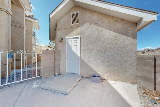 property entrance featuring visible vents, stucco siding, and fence