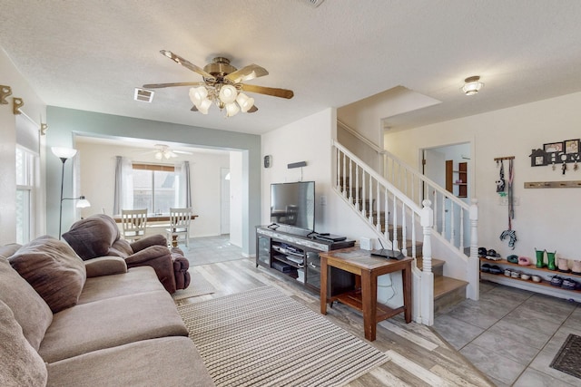 living room with light wood finished floors, visible vents, ceiling fan, stairs, and a textured ceiling