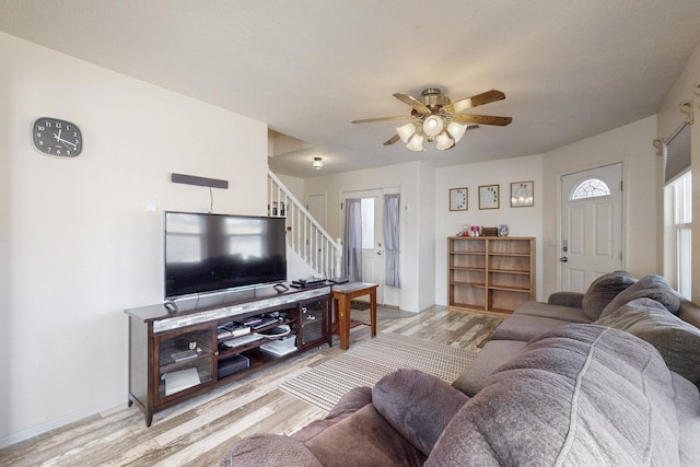 living room with baseboards, light wood-style floors, ceiling fan, and stairs