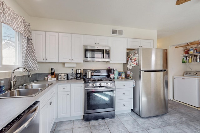 kitchen featuring visible vents, stainless steel appliances, white cabinets, washer / clothes dryer, and a sink