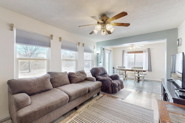 living area featuring baseboards, a textured ceiling, light wood-style flooring, and a ceiling fan