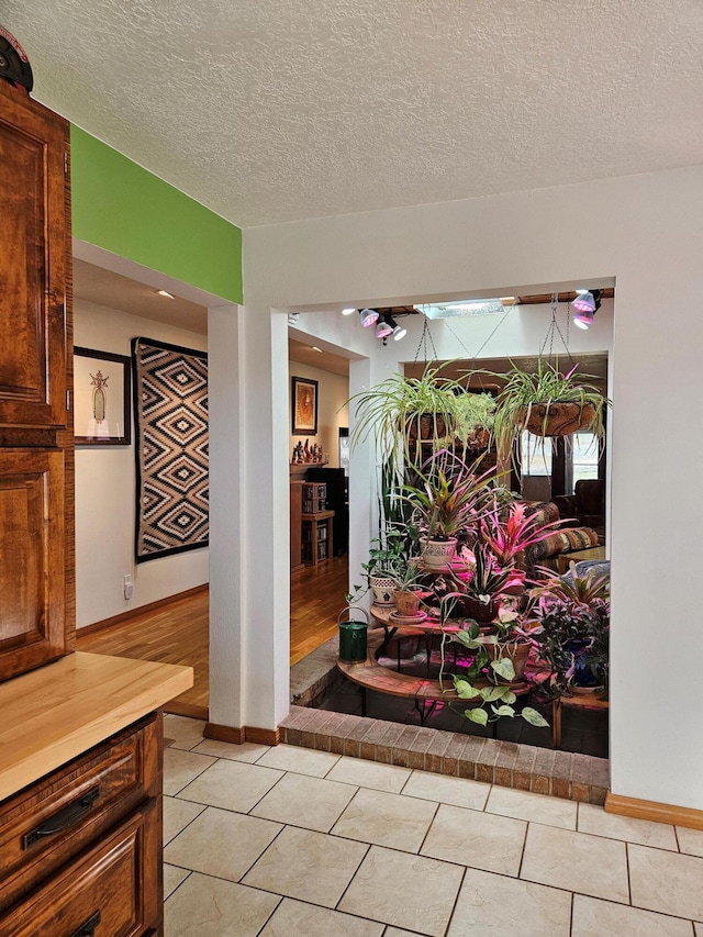 interior space featuring light tile patterned flooring, a textured ceiling, and baseboards