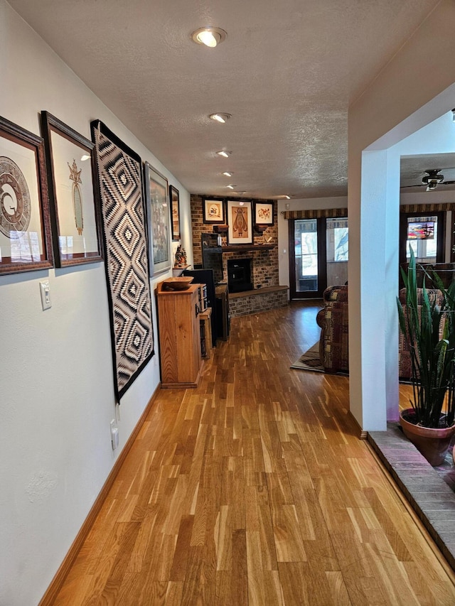 hall with a textured ceiling, baseboards, and wood finished floors