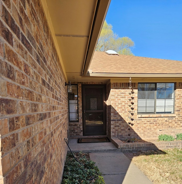 entrance to property with brick siding and a shingled roof