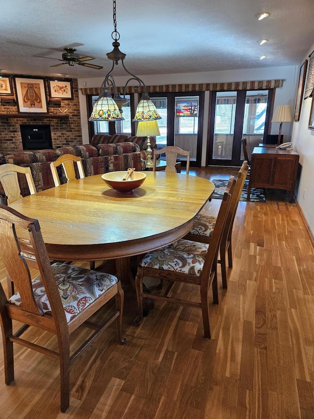 dining room featuring a brick fireplace, ceiling fan, and wood finished floors