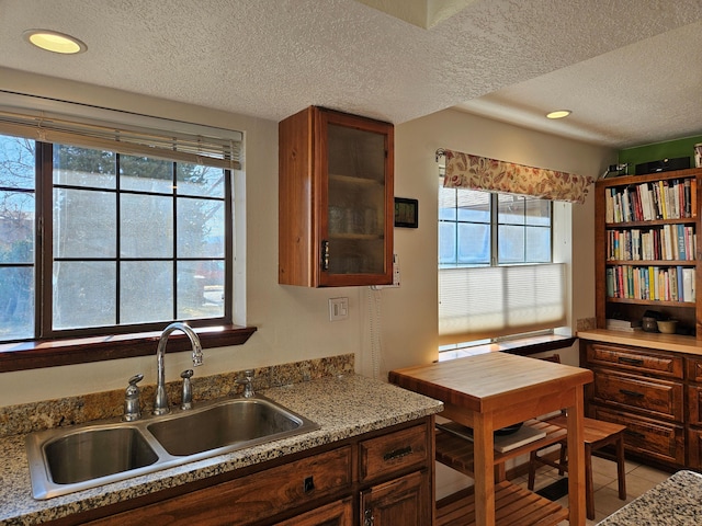 kitchen featuring a sink, a textured ceiling, light tile patterned flooring, light countertops, and glass insert cabinets