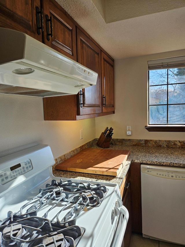 kitchen with white appliances, dark countertops, under cabinet range hood, and a textured ceiling