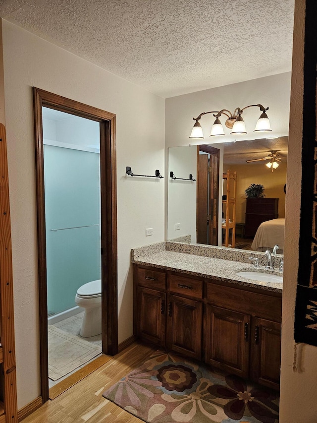 bathroom with connected bathroom, ceiling fan, toilet, wood finished floors, and vanity