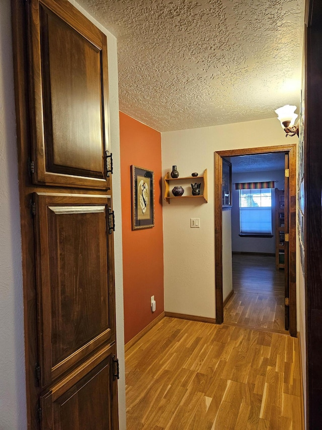 hallway with light wood-style flooring, baseboards, and a textured ceiling