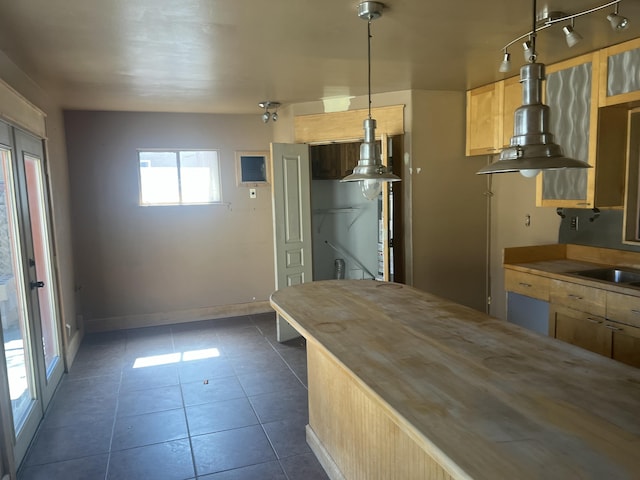 kitchen with baseboards, wooden counters, dark tile patterned flooring, a sink, and pendant lighting