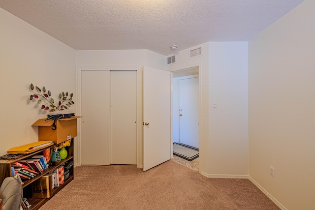 interior space featuring light carpet, visible vents, a textured ceiling, and a closet