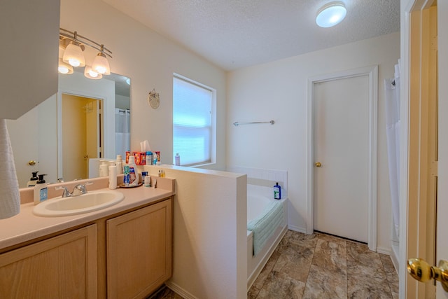 bathroom with a textured ceiling, a bath, and vanity