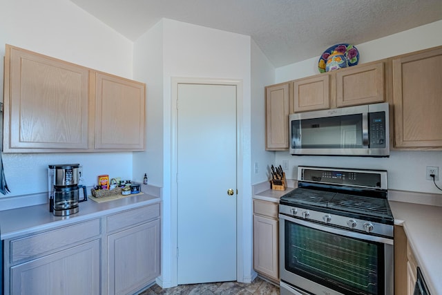 kitchen featuring a textured ceiling, light countertops, light brown cabinetry, and stainless steel appliances