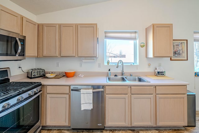 kitchen with light brown cabinets, lofted ceiling, a sink, stainless steel appliances, and light countertops