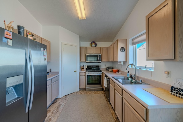 kitchen with light brown cabinets, a sink, a textured ceiling, stainless steel appliances, and light countertops