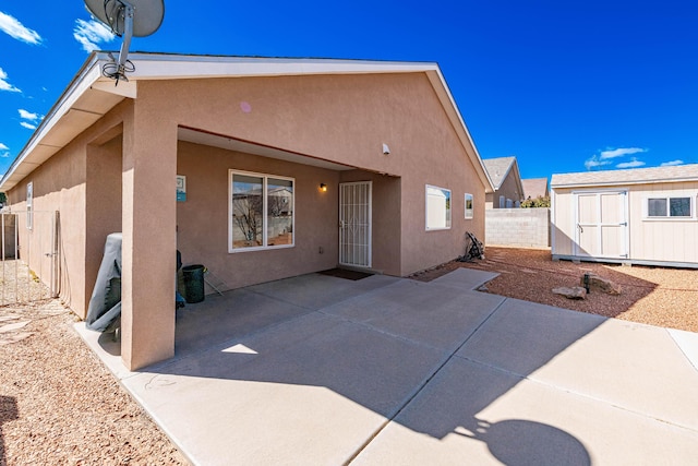 rear view of house featuring stucco siding, a patio, an outdoor structure, and a shed