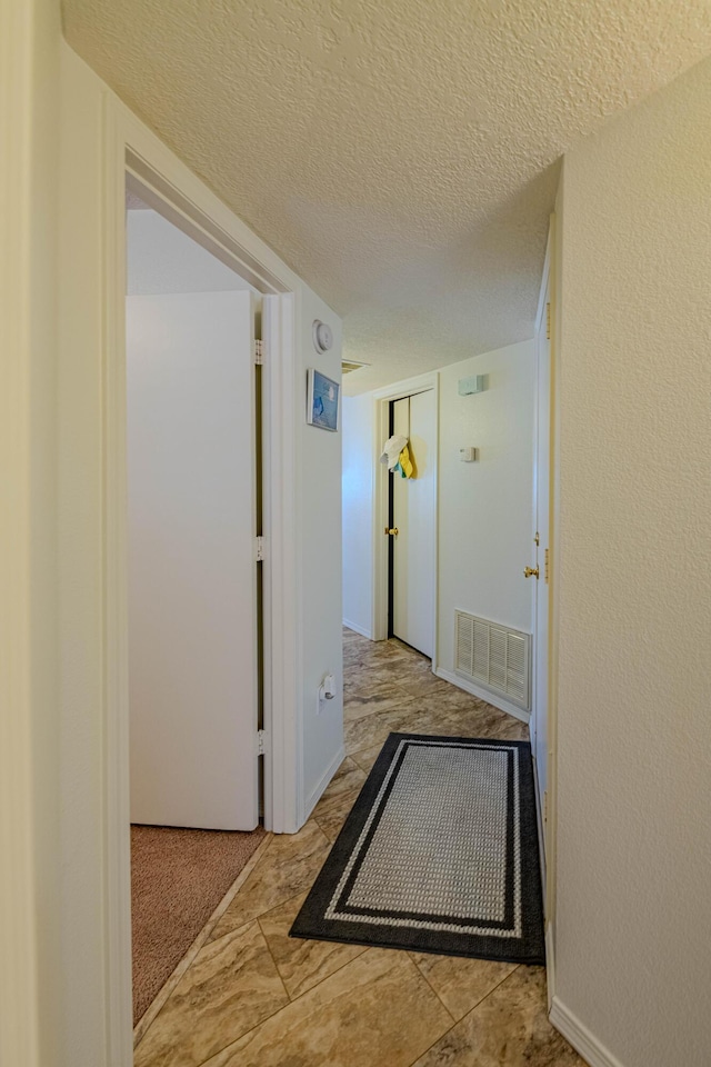 hall with visible vents, carpet floors, and a textured ceiling