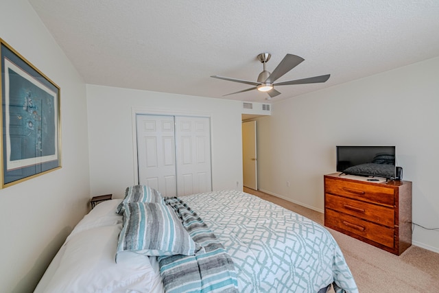 bedroom featuring visible vents, light colored carpet, a closet, a textured ceiling, and a ceiling fan