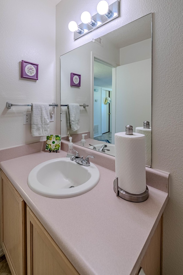 bathroom featuring vanity, a textured wall, and visible vents