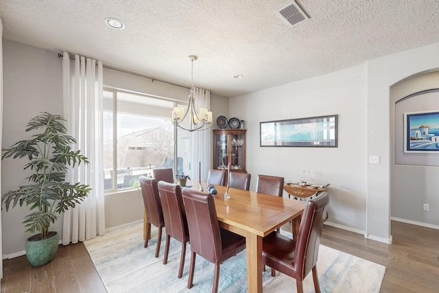 dining room featuring visible vents, baseboards, a chandelier, light wood-type flooring, and a textured ceiling