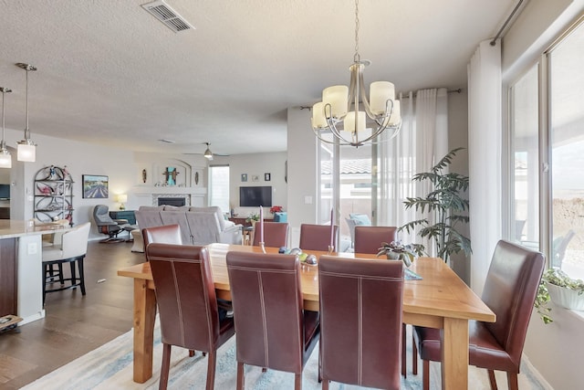 dining room with wood finished floors, visible vents, a fireplace, a textured ceiling, and ceiling fan with notable chandelier