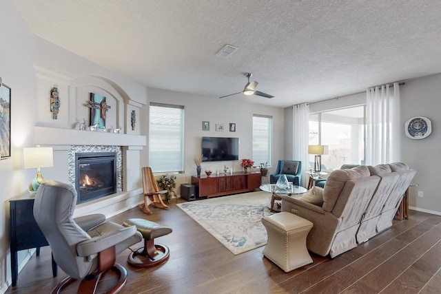 living area with visible vents, ceiling fan, dark wood finished floors, a tiled fireplace, and a textured ceiling