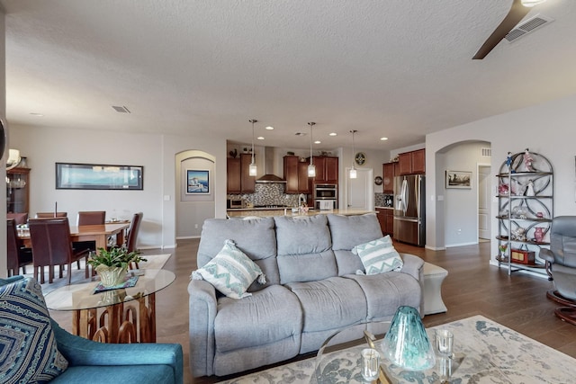 living area with visible vents, dark wood-type flooring, recessed lighting, arched walkways, and a textured ceiling