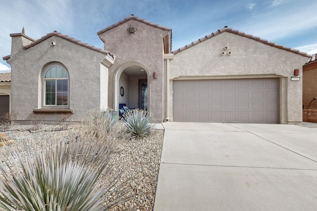 mediterranean / spanish house featuring stucco siding, an attached garage, a tile roof, and concrete driveway