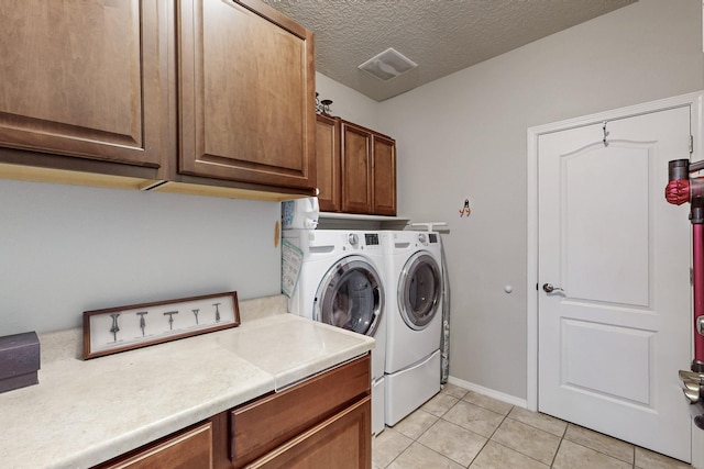 clothes washing area featuring visible vents, washing machine and dryer, light tile patterned floors, cabinet space, and a textured ceiling