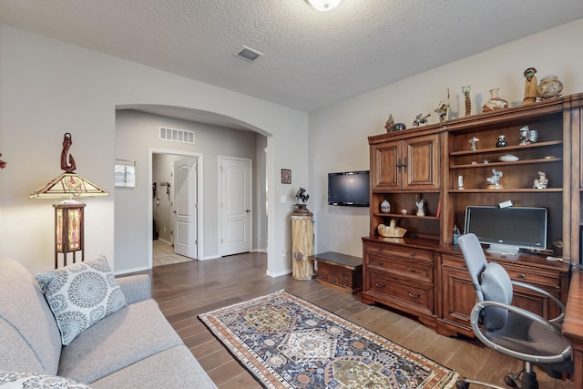 office with wood finished floors, arched walkways, visible vents, and a textured ceiling