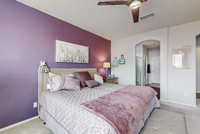 carpeted bedroom featuring visible vents, arched walkways, a textured ceiling, and baseboards