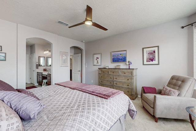 bedroom with visible vents, light carpet, arched walkways, a textured ceiling, and a ceiling fan