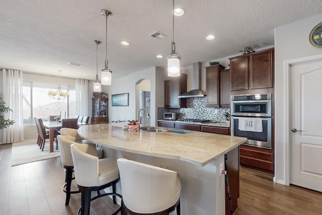 kitchen featuring tasteful backsplash, visible vents, wall chimney range hood, appliances with stainless steel finishes, and arched walkways