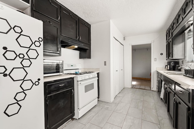 kitchen featuring refrigerator, white range with gas stovetop, a sink, under cabinet range hood, and dark cabinets