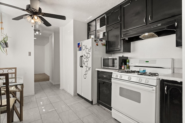 kitchen with ceiling fan, under cabinet range hood, light countertops, white appliances, and dark cabinets