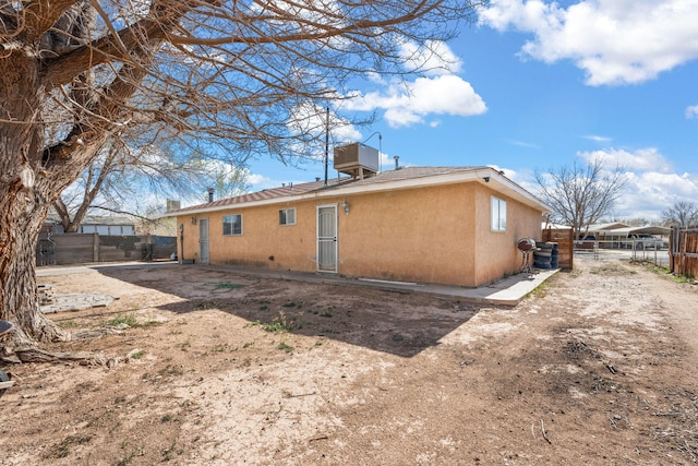 back of property with stucco siding, central AC, and fence