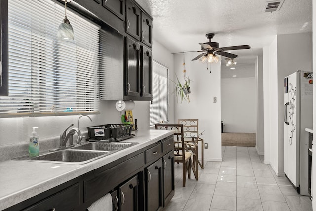 kitchen featuring visible vents, freestanding refrigerator, ceiling fan, a sink, and dark cabinets