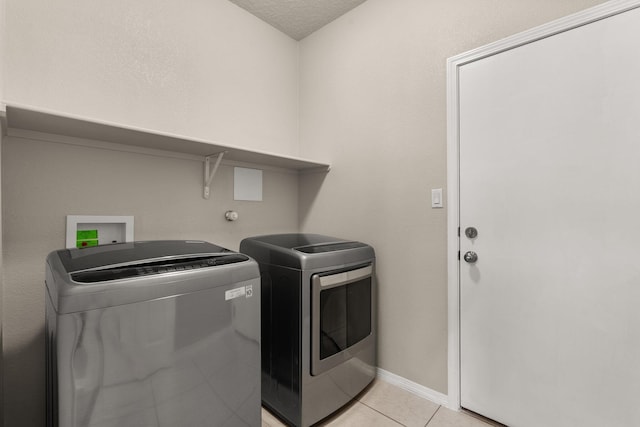 washroom with light tile patterned floors, baseboards, washing machine and clothes dryer, laundry area, and a textured ceiling