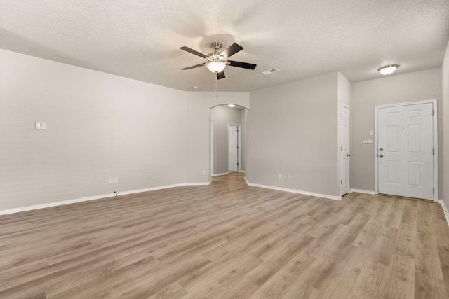 unfurnished room featuring a ceiling fan, a textured ceiling, arched walkways, light wood-style floors, and baseboards